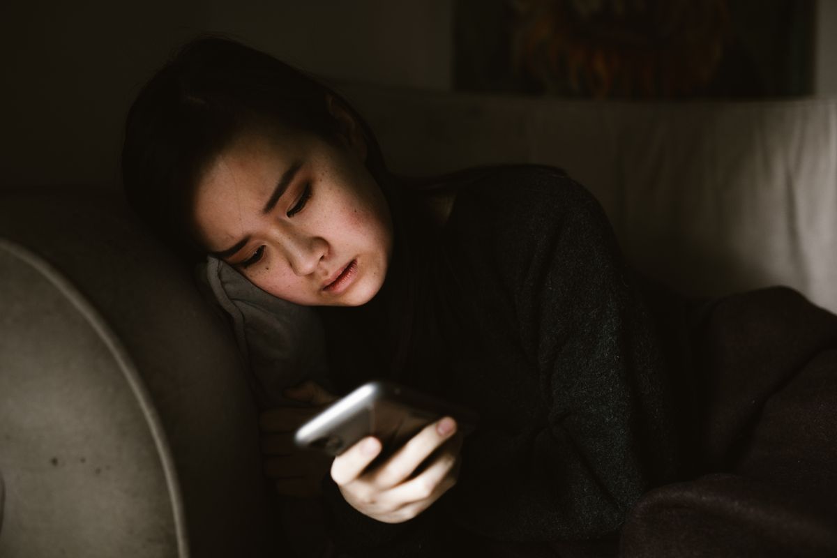 Young woman checking her phone on a couch in the evening, a reminder to set limits on sweepstakes play