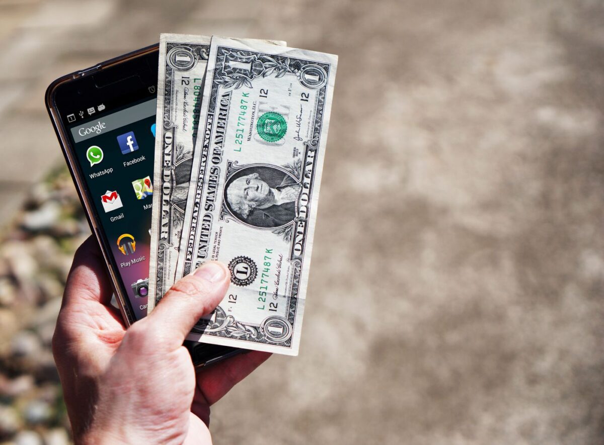 US dollar bills held next to a smartphone, representing a completed casino payout