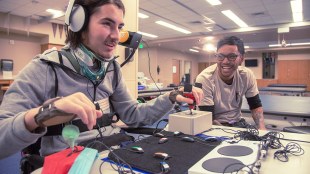 a person plays a video game using an xbox adaptive controller with accessibility option while another person looks on